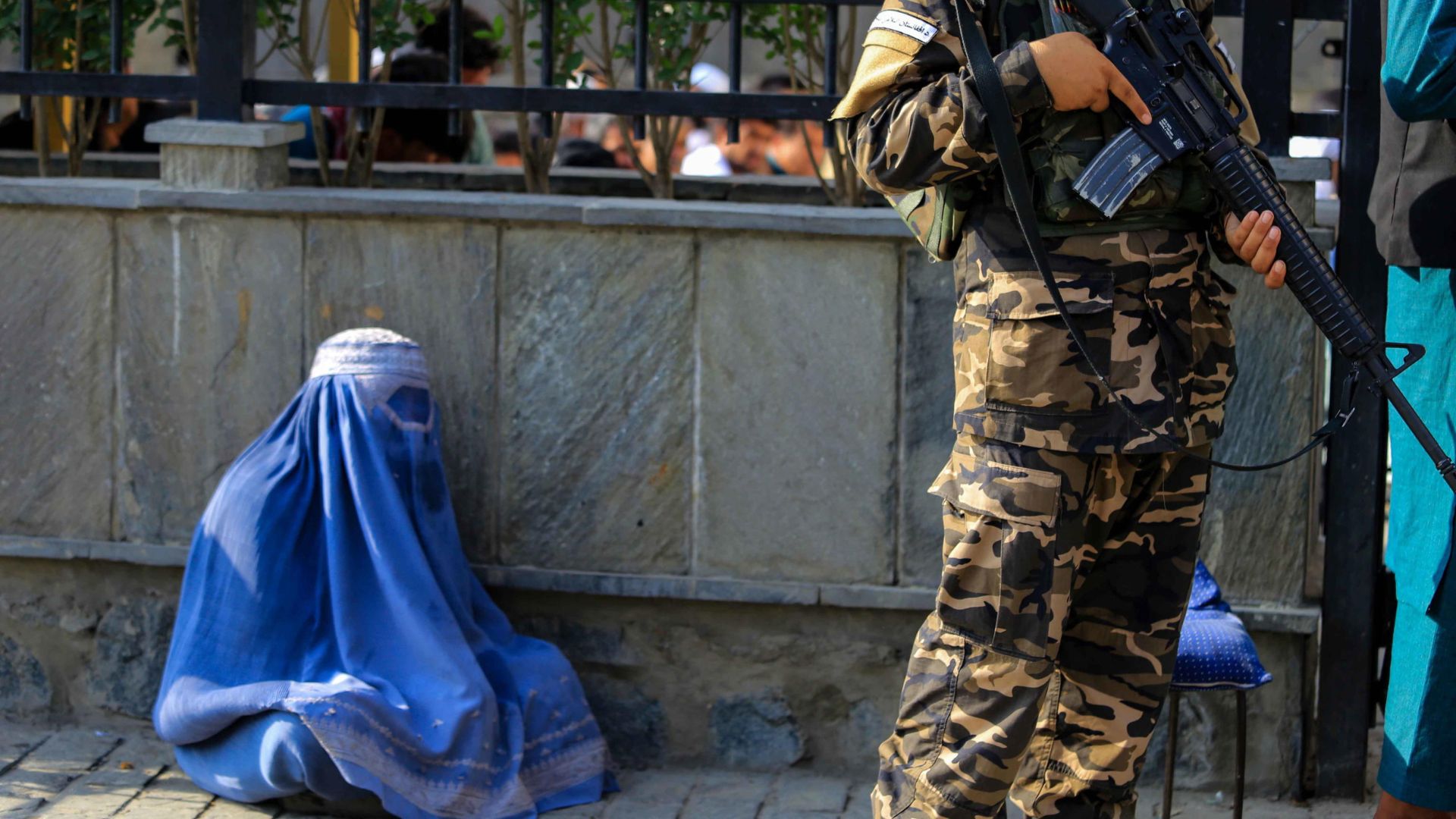 Afghanistan - Una donna afgana, con indosso il burqa, chiede l'elemosina mentre i talebani fanno la guardia in un luogo pubblico a Kabul, Afghanistan, il 27 luglio 2022.